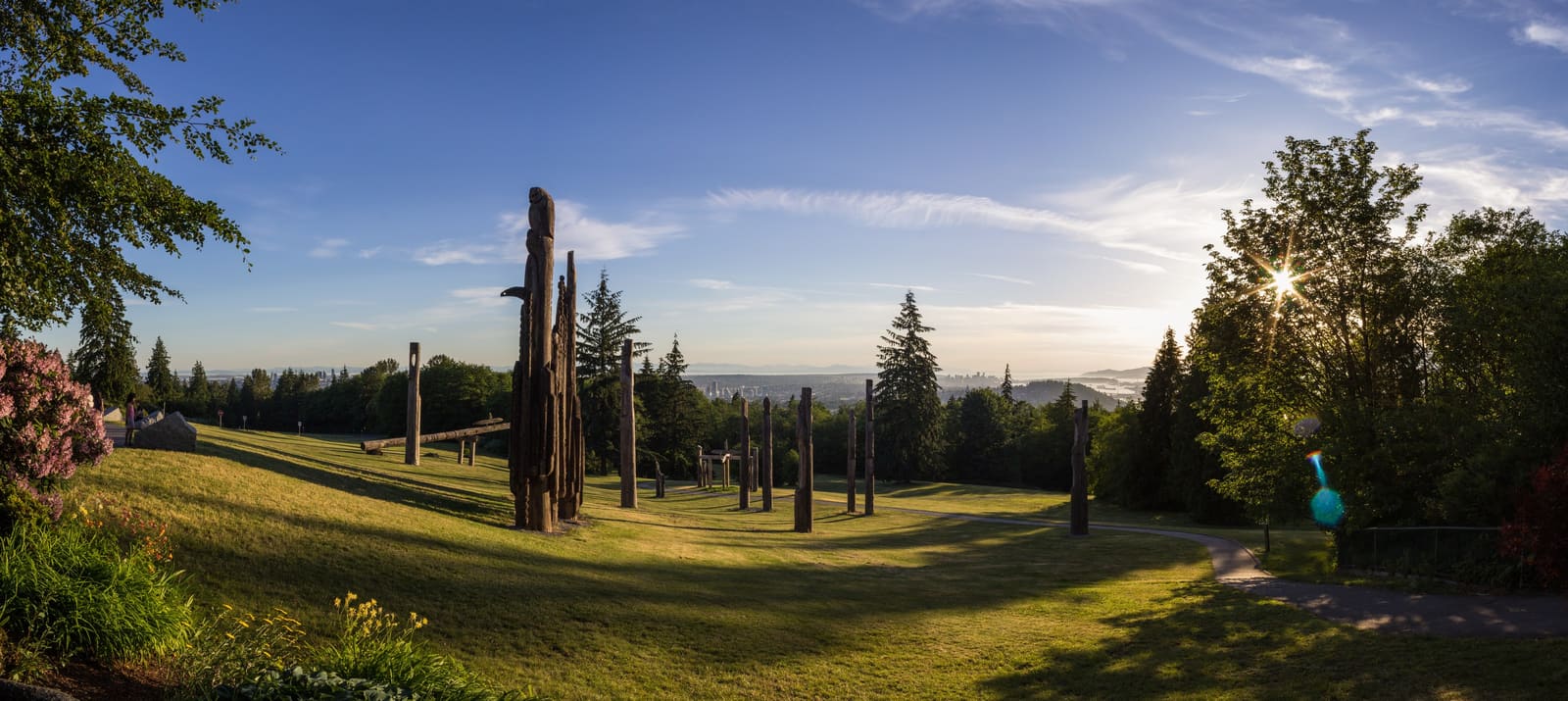 Carved wooden poles on a grassy hillside at sunrise, with the Metro Vancouver skyline in the distance